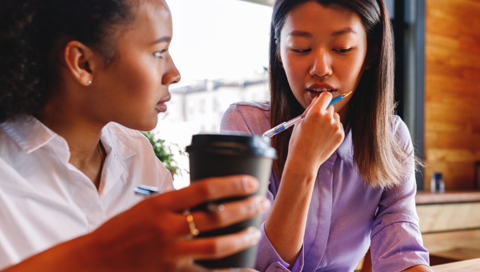 2 students talking as they drink coffee and look at school materials