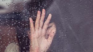 woman with hand up behind a rainy piece of glass