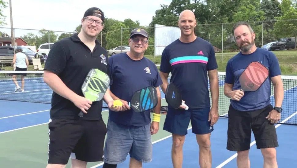 4 men holding pickleball gear