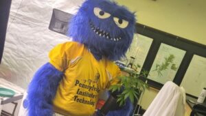 A mascot holds a cannabis plant in the Pennsylvania Institute of Technology grow lab