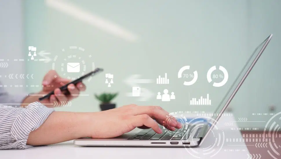 person types on laptop holding phone with digital marketing graphics in air