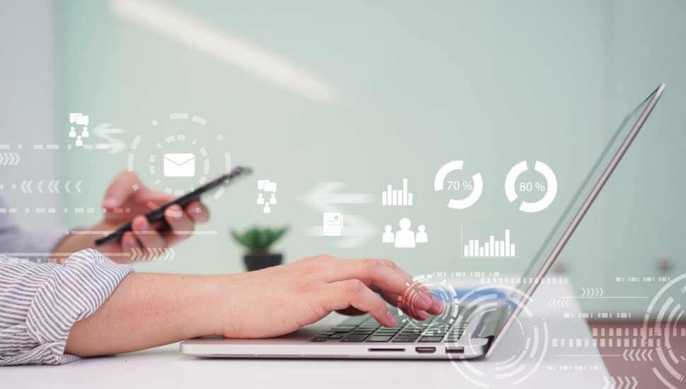 person types on laptop holding phone with digital marketing graphics in air