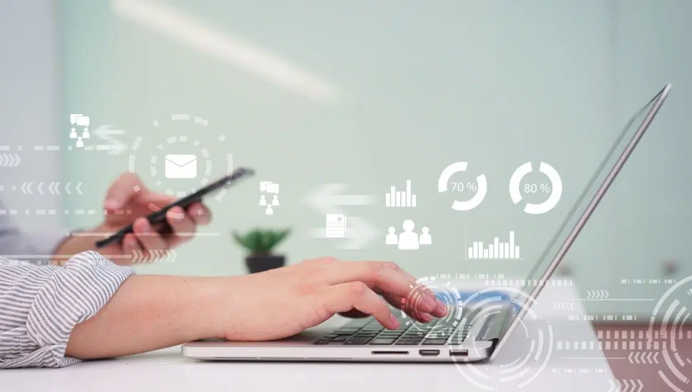 person types on laptop holding phone with digital marketing graphics in air