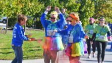 Volunteer sprays two participants with colored powder at 5K Color Run