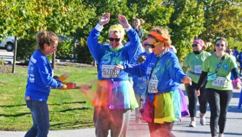 Volunteer sprays two participants with colored powder at 5K Color Run