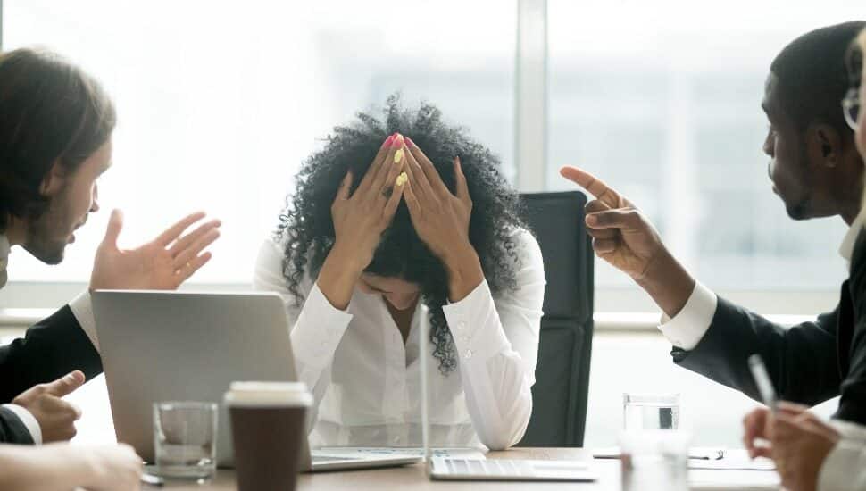 Upset depressed black woman leader suffering from gender discrimination inequality at work, diverse men colleagues pointing fingers scolding bullying frustrated african businesswoman at workplace