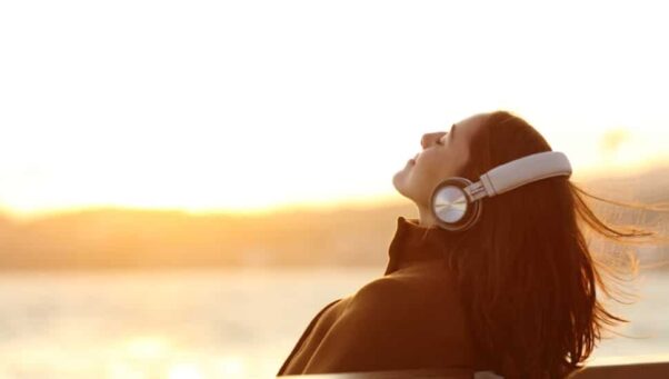 A woman with headphones by the water at sunset