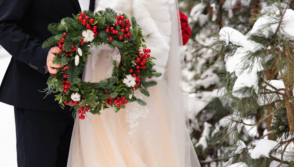 Winter wedding. Bride and groom holding Christmas wreath
