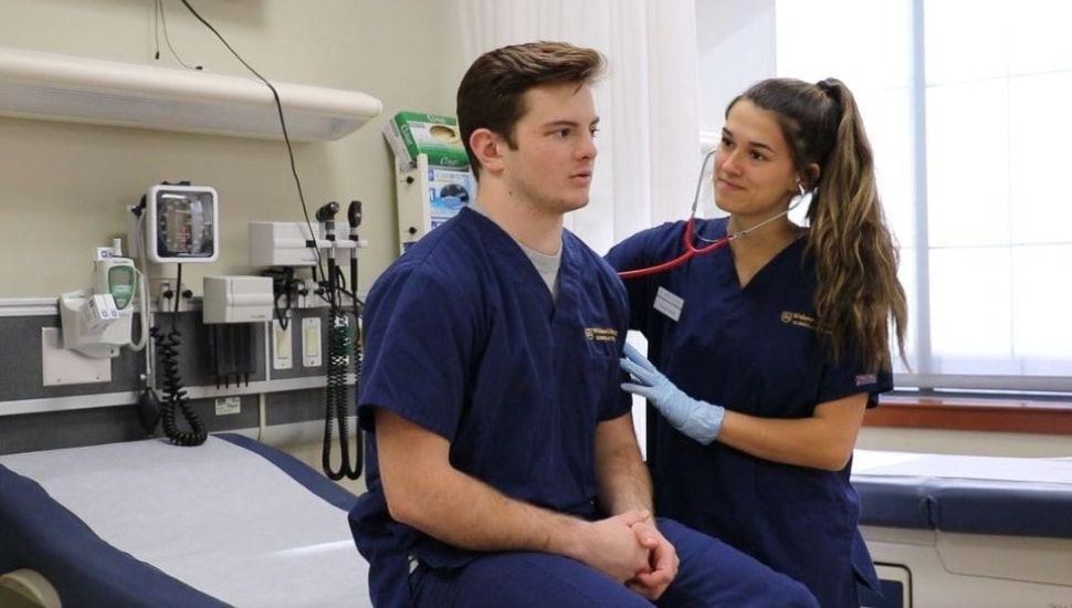 A female nursing student performs a hands-on assessment on a male classmate in the nursing simulation lab at Widener University