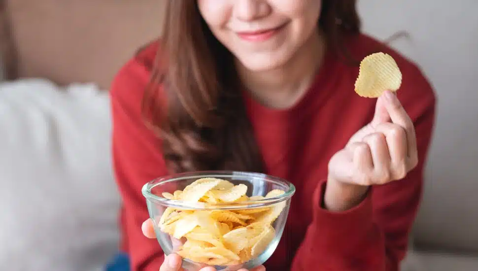 Closeup image of a young woman picking and eating potato chips at home