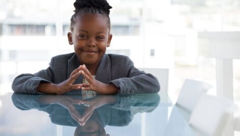 A smiling young Black child with hand clasped sitting at a table