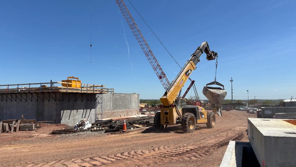 A crane lifts a large concrete structure at the Lock 57 Water Treatment Plant construction site, with workers and materials visible in the background.