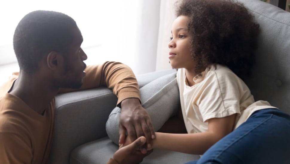 A father talking gently to his seated daughter