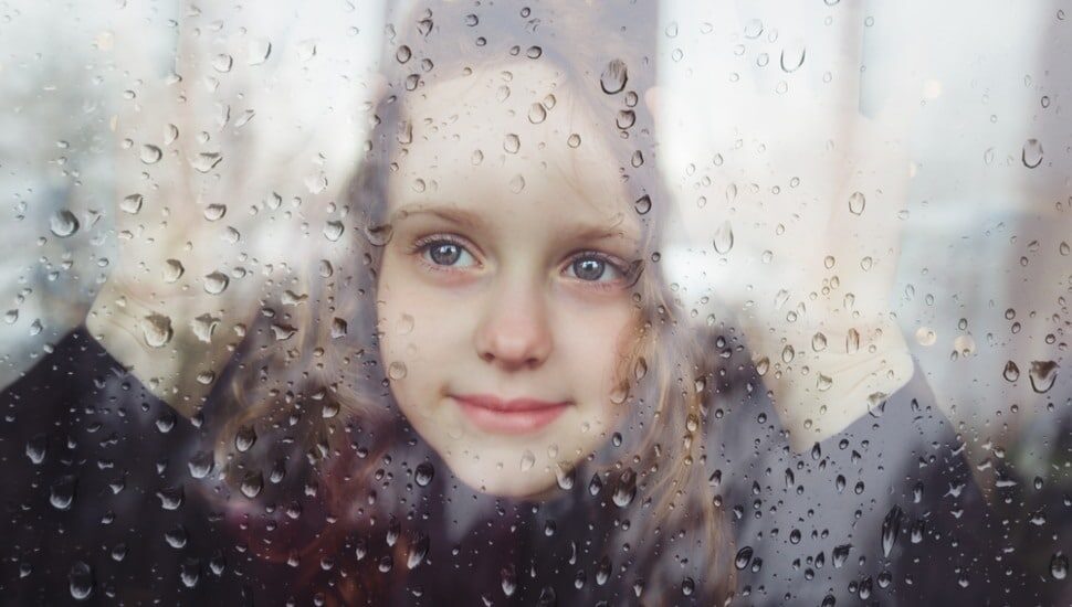 A sad little girl looking out of a window on a rainy day