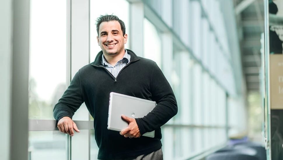 A smiling man holding a laptop inside