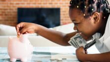A little girl holding cash putting coins into a piggy bank