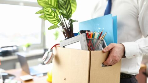 person getting laid off carrying box full of desk items in office