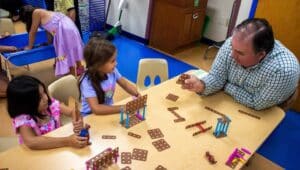 Representative John Lawrence sitting at table playing with building blocks with two young girls