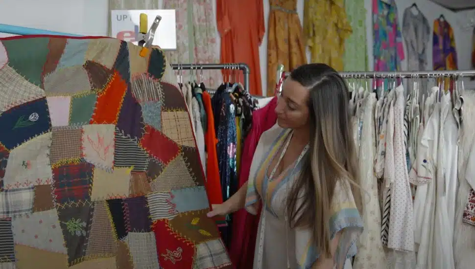 Malena Martinez holding quilt and standing in front of rack of vintage clothing at Malena's Vintage Boutique in West Chester