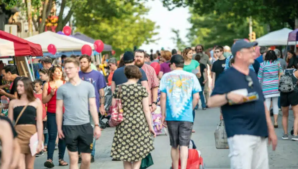 Phoenixville residents walking down sidewalk at event with vendor tents in background