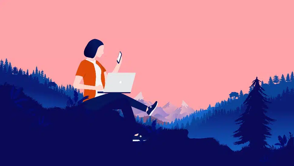Person with computer and phone working in nature landscape, with forest and mountains in background. flexible work