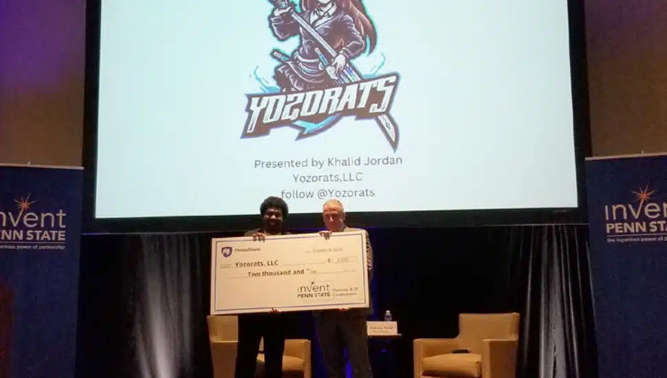 Khalid Jordan holds a large check for ,000 with an Invent Penn State representative.