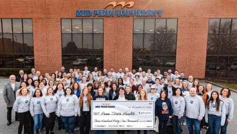 Members of Mid Penn Bank’s “No Shave November” team with giant check in front of "Mid Penn University" building
