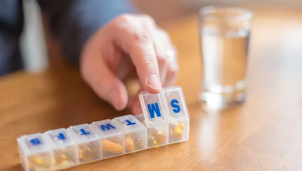 man's hand closing a pill case for daily vitamins