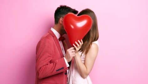 Affectionate couple covering face with balloon and kissing