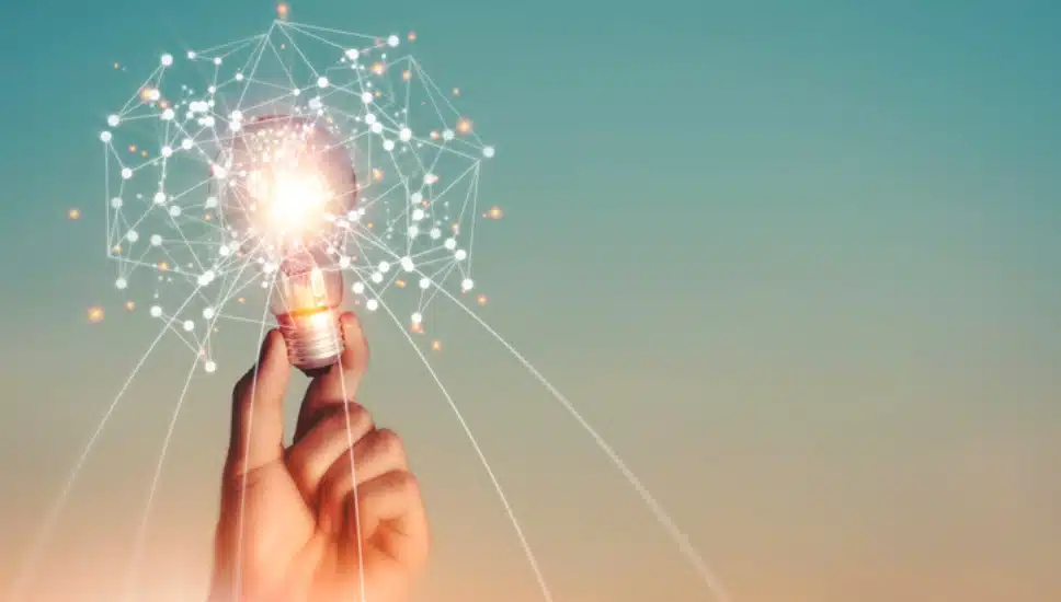 A hand holds an illuminated light bulb.