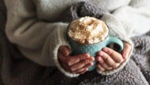 Woman with blanket warming her hands in mug of hot chocolate with whipped cream