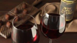 Glasses of red wine with chocolate candies on wooden table