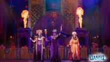 still image of three actors in costume on stage in front of flames