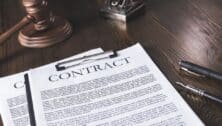 A printed out contract on a desk with two pens and a gavel.