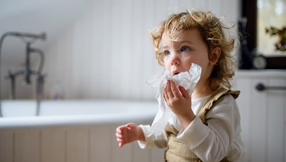 Small sick girl with cold at home sitting on ground, blowing nose.