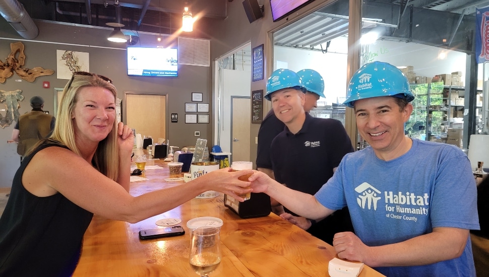 Attendees of Habitat for Humanity of Chester County's previous "Pints with a Purpose" Happy Hour holding pints of beer gathered at a table.