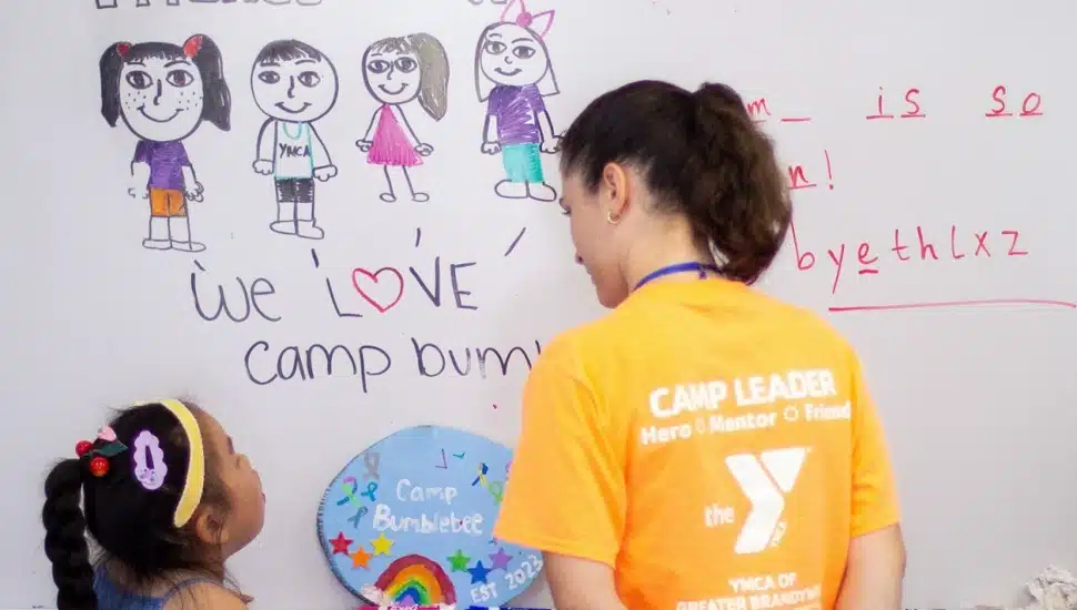 A YGBW camp counselor draws on a whiteboard with a camper at BumbleBee Day Camp at the Upper Main Line Branch in Berwyn during the summer of 2023.
