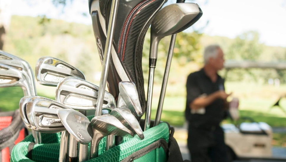 A close up of a golf bag filled with clubs and a golfer in the background.