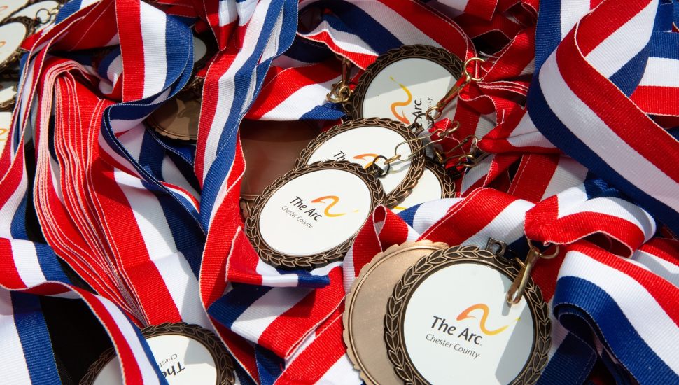 A pile of red, white and blue ribbons with The Arc of Chester County logo.