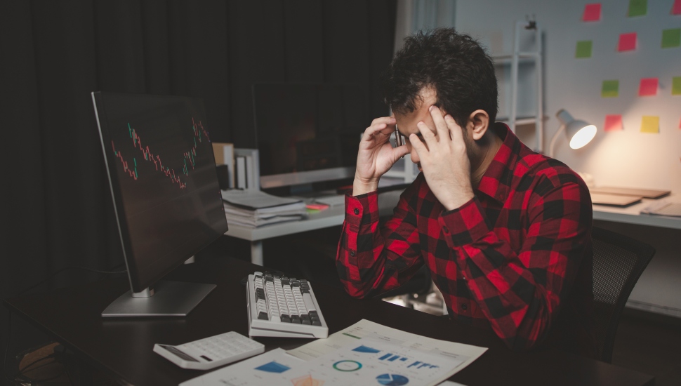 Man stressed out/tired looking at investment option by his computer.
