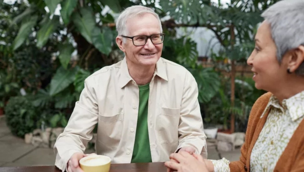 Seniors sitting outside with coffee, talking.