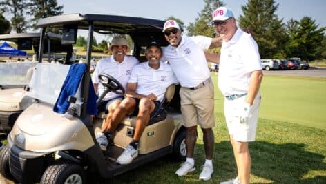 Four players at golf classic in golf cart on course