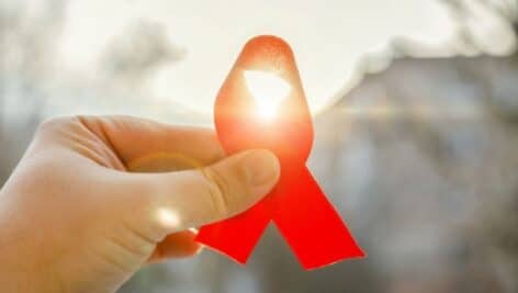 A hand holding a glowing red ribbon, the international symbol of awareness and support for people living with HIV/AIDS/