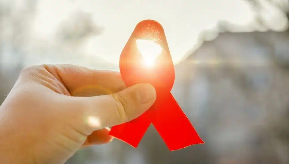 A hand holding a glowing red ribbon, the international symbol of awareness and support for people living with HIV/AIDS/