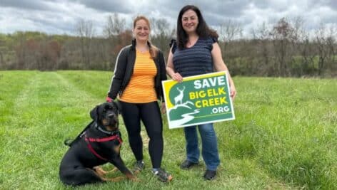 two women with dog holding big elk poster