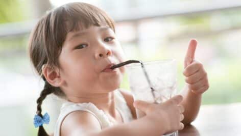 Little girl drinking water out of cup with a straw.