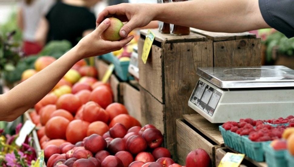 Picture of produce at farmers market with outstretched hand holding apple.