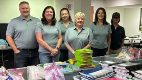 The Brumbaugh Wealth Management team gathers at a table to pack backpacks at Home of the Sparrow.