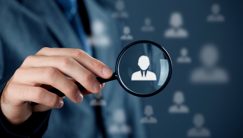 magnifying glass hovering over outlines of professionals in suits.