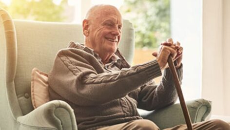 A smiling older gentleman with a cane sitting in a chair